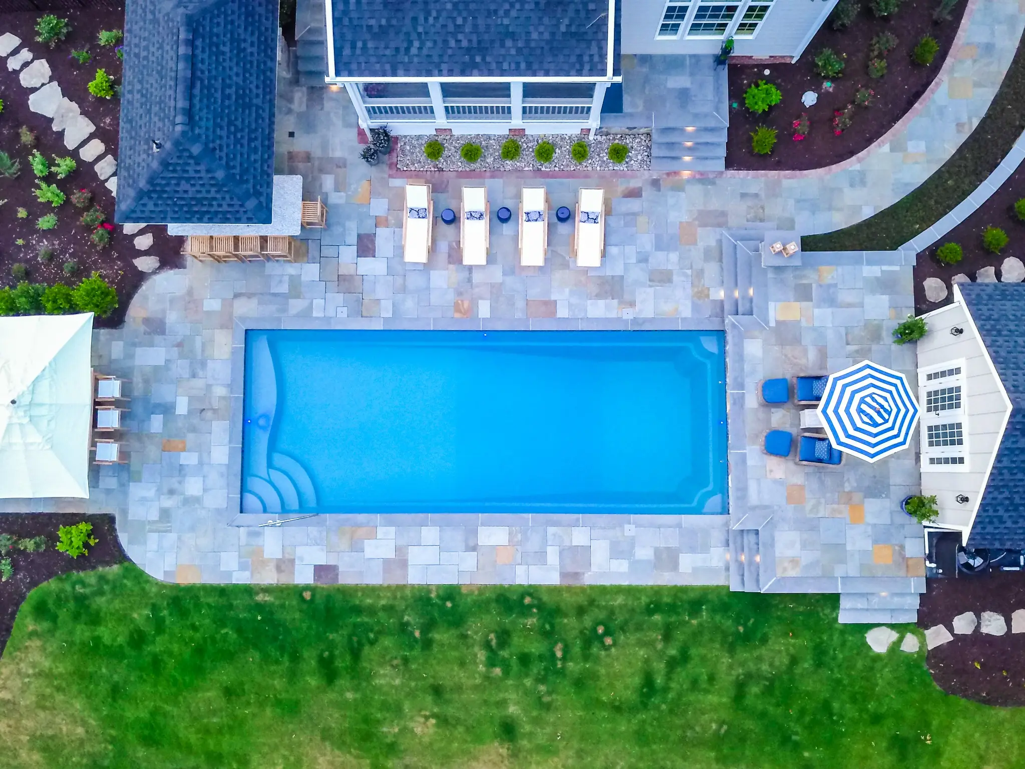 Overhead view of a rectangular pool, paver patio, lounge seating, and outdoor bar pavilion