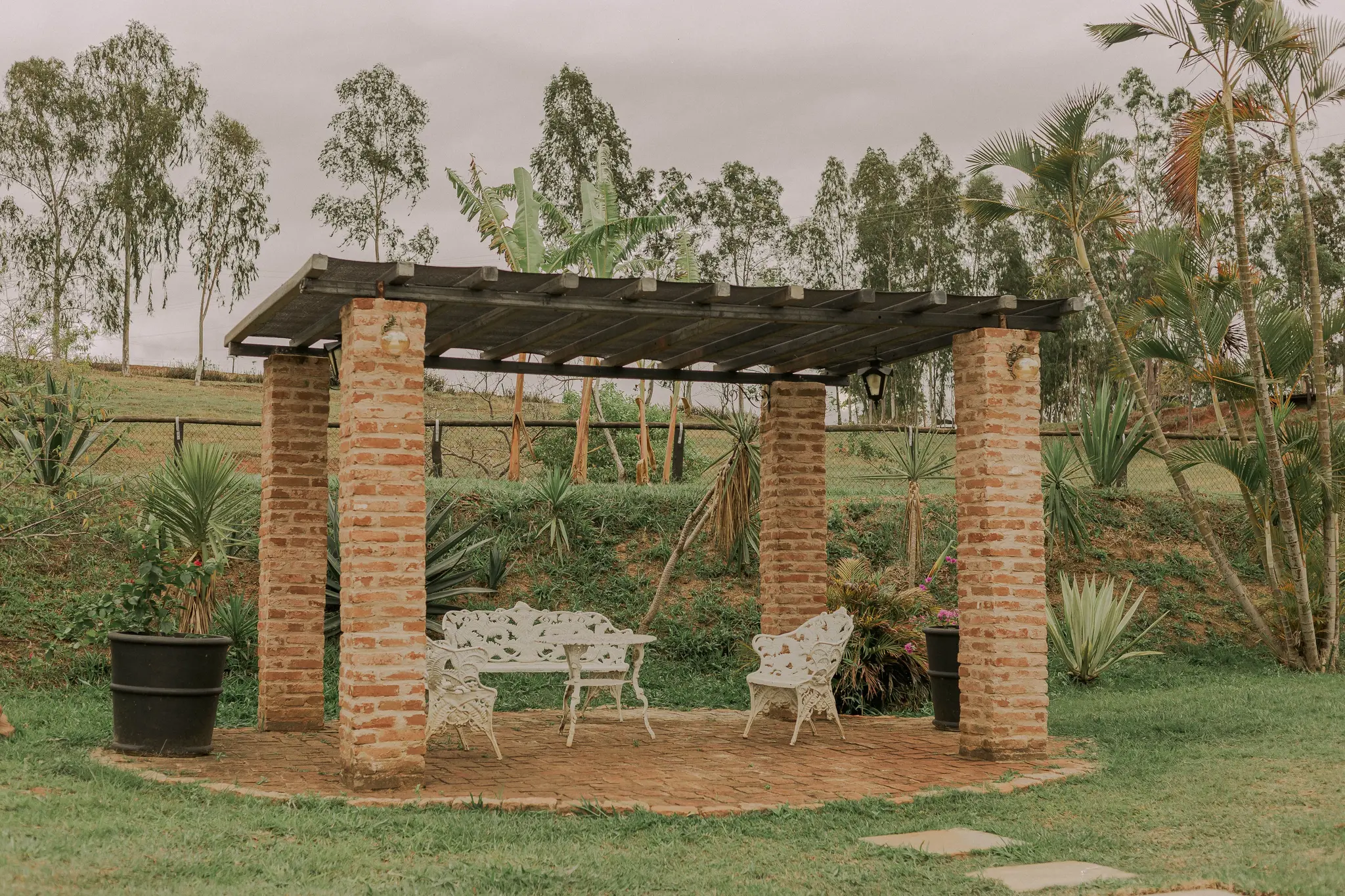 Garden pergola with brick columns, open wood rafters, and white seating